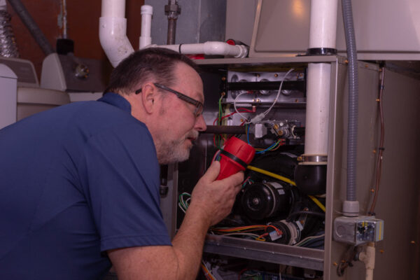A technician inspecting the internals of a gas furnace heater with a flash light